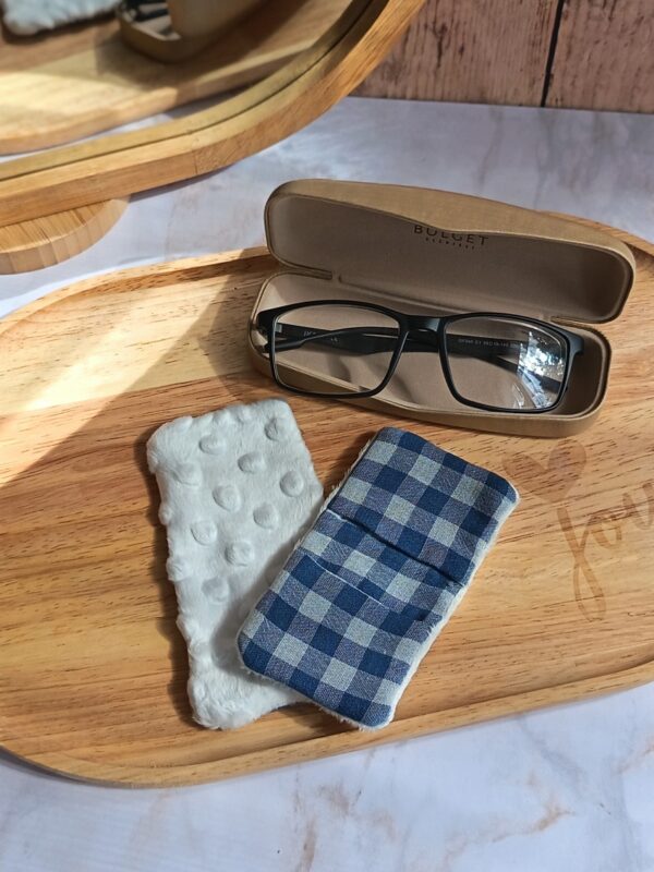 Gros plan sur un essuie-lunettes tissu double gaze vichy bleu et blanc, posé à côté de sa face minky blanche sur un plateau en bois.
