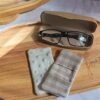 Plateau en bois avec un étui à lunettes ouvert et un essuie-lunettes artisanal réversible double gaze vichy lin et minky blanc, sous une lumière douce.