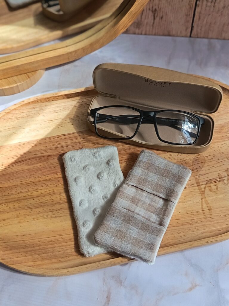 Plateau en bois avec un étui à lunettes ouvert et un essuie-lunettes artisanal réversible double gaze vichy lin et minky blanc, sous une lumière douce.