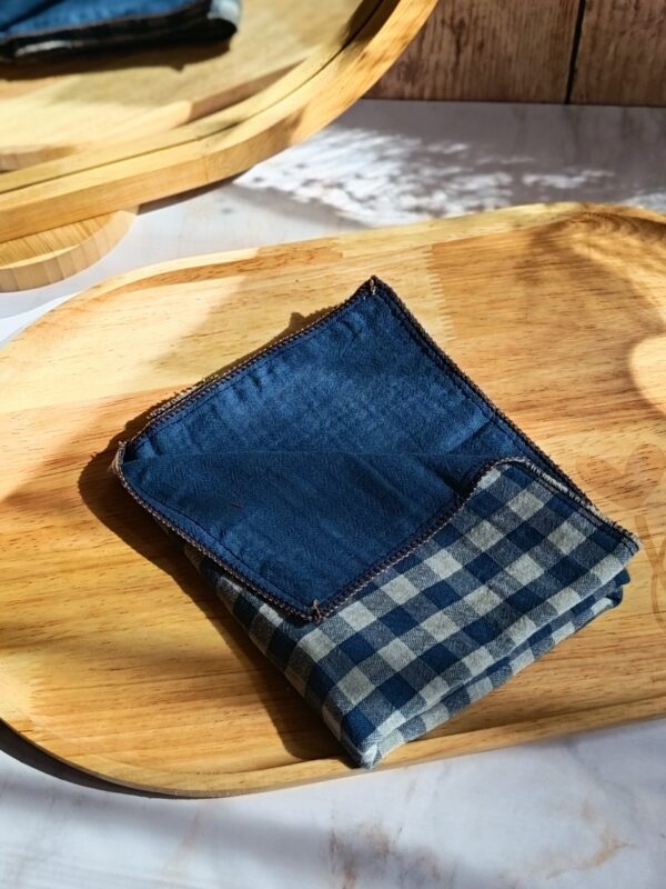 Mouchoir tissu double gaze artisanal plié avec soin, révélant le motif vichy bleu sur un plateau en bois ensoleillé.