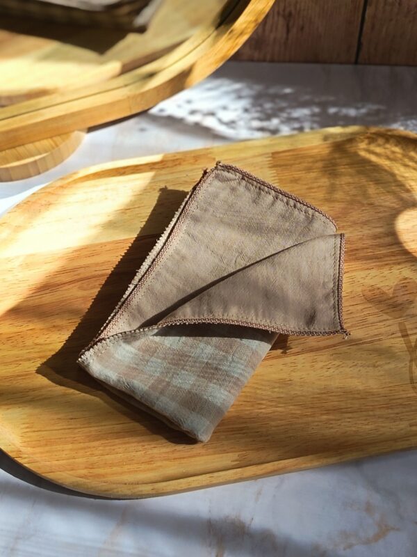 Mouchoir tissu double gaze plié en carré, motif vichy lin, prêt à être glissé dans une poche, sur un plateau en bois.