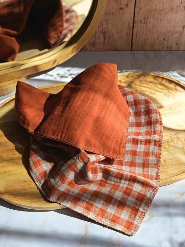 Mouchoir tissu double gaze vichy terracotta Malili_fée, déplié sur un plateau en bois pour exposer sa couleur chaude et sa texture aérienne.