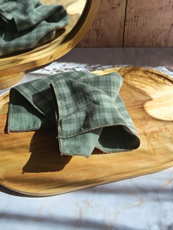 Mouchoir tissu double gaze artisanal Malili_fée, coloris vichy vert pastel, déplié sur un plateau en bois.