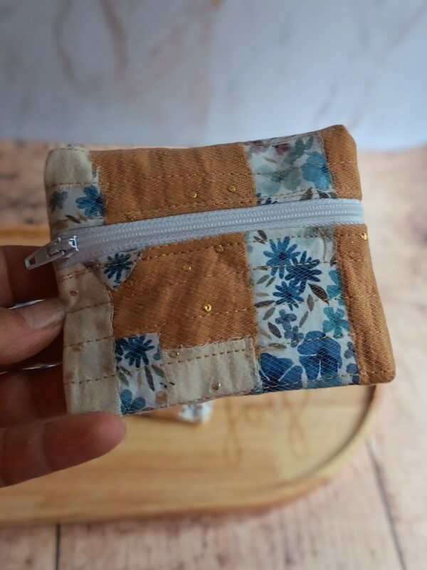 Gros plan sur un petit porte-monnaie artisanal bicolore associant un coton fleuri bleu et un tissu nid d'abeille ocre, tenu en main.
