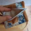 Vue d'un petit porte-monnaie artisanal ouvert rempli de pièces de monnaie, montrant sa doublure en tissu bleu et sa fermeture éclair robuste.
