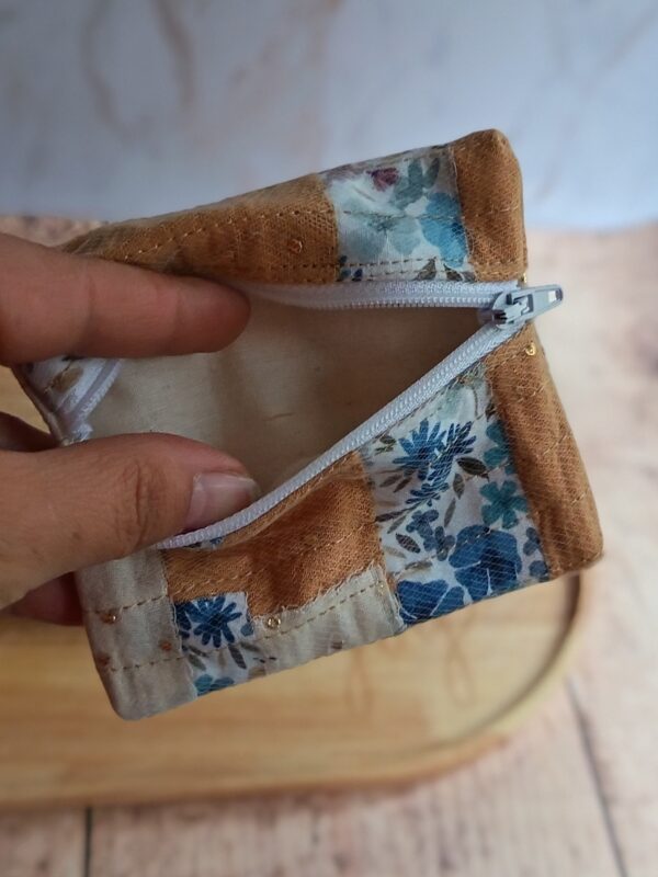 Vue d'un petit porte-monnaie artisanal ouvert rempli de pièces de monnaie, montrant sa doublure en tissu bleu et sa fermeture éclair robuste.