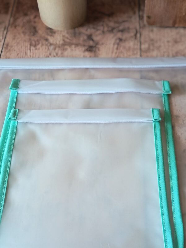 Gros plan sur les finitions et les coutures régulières de deux sacs de congélation écologiques lavables. On observe le biais en tissu vert menthe parfaitement posé sur les bords du film EVA étanche.