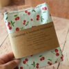 Emballage à sandwich réutilisable blanc à motif cerises rouges, entouré de son bandeau de présentation en papier kraft recyclé. Le bandeau affiche fièrement le nom du produit, la marque "Malili_fee" ainsi que les conseils d'utilisation pratiques.