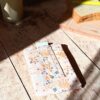 Zoom sur la variation de l'emballage à sandwich réutilisable en tissu floral rose poudré et saumon. Le produit est fermé par sa bande scratch et présenté dans un décor de cuisine lumineux.