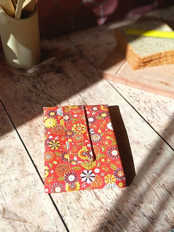 Emballage à sandwich réutilisable lavable avec son motif de fleurs japonaises rouge, jaune et ocre. Présentation du produit plié au format compact pour la miniature de variation.