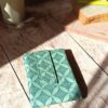 Emballage à sandwich réutilisable et imperméable décliné en coton enduit vert sauge avec un motif géométrique de rosaces et de lignes fines.