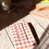 Emballage à sandwich lavable en tissu au motif grands carreaux vichy orange, blanc et gris pastel, fermé de manière compacte.