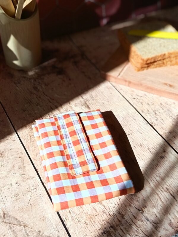 Emballage à sandwich lavable en tissu au motif grands carreaux vichy orange, blanc et gris pastel, fermé de manière compacte.