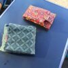 Gros plan sur deux emballages à sandwich réutilisables pliés, posés côte à côte sur une table de camping bleue. L'un est en coton enduit rouge à motif floral coloré, l'autre est vert avec un motif géométrique discret. On voit clairement les étiquettes en tissu "Malili_fee" cousues sur chaque emballage.