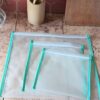 Présentation à plat d'un lot de trois sacs de congélation réutilisables de tailles différentes. Le film EVA translucide laisse deviner le plan de travail en bois tandis qu'un biais de couleur vert menthe borde soigneusement chaque modèle.