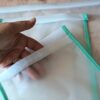 Vue rapprochée d'une main tenant la bande agrippante d'un sac de congélation réutilisable. La transparence du film plastique EVA laisse voir les doigts de la créatrice à travers la matière souple.