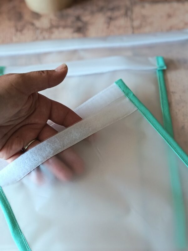 Vue rapprochée d'une main tenant la bande agrippante d'un sac de congélation réutilisable. La transparence du film plastique EVA laisse voir les doigts de la créatrice à travers la matière souple.