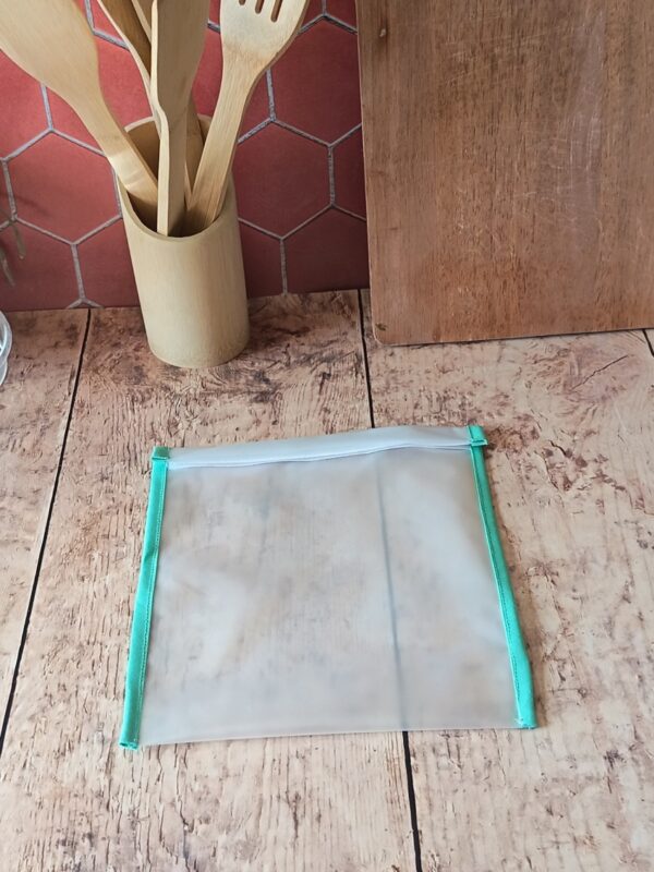 Le sac de congélation réutilisable de taille M ($21 \times 23\text{ cm}$) présenté seul à plat sur une table en bois. Le biais vert menthe apporte une touche décorative et soignée à cet accessoire écoresponsable.