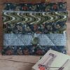Vue de face d'une housse de livre de poche en tissu matelassé gris avec rabat graphique et bouton de fermeture.