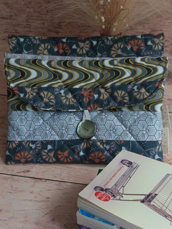 Vue de face d'une housse de livre de poche en tissu matelassé gris avec rabat graphique et bouton de fermeture.