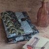 Housse de livre de poche en tissu matelassé gris aux motifs japonais et vagues, posée près d'un livre et d'un soliflore.
