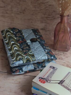 Housse de livre de poche en tissu matelassé gris aux motifs japonais et vagues, posée près d'un livre et d'un soliflore.