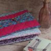 Pile de housses et pochette à livre de poche artisanale en tissu matelassé aux tons rose, fuchsia et prune.