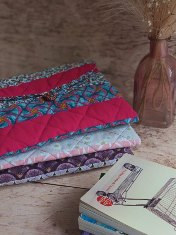 Pile de housses et pochette à livre de poche artisanale en tissu matelassé aux tons rose, fuchsia et prune.