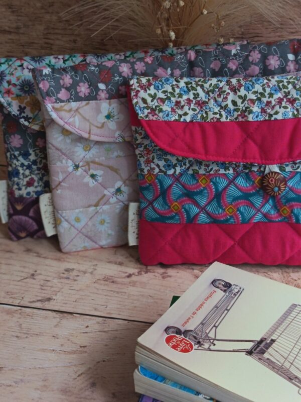 Pochette à livre de poche artisanale matelassée rose fuchsia en premier plan sur un lot de housses florales.