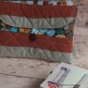 Pochette à livre de poche écoresponsable en tissu matelassé terracotta et beige, posée près de livres sur une table en bois.
