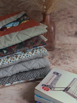 Pile de plusieurs pochettes à livre de poche écoresponsables matelassées aux tons neutres, terracotta et beige.
