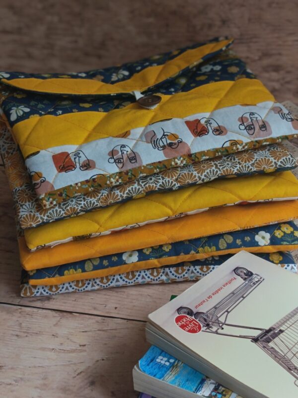 Pile de housses et pochette à livre de poche en tissu aux imprimés géométriques, floraux et graphiques jaunes et bleus.