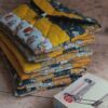 Pochette à livre de poche en tissu matelassée jaune moutarde et bleu nuit, posée sur une pile avec des livres.