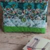 Pochette à livre de poche faite main en tissu matelassé vert et motifs feuillage avec bouton de fermeture et pile de livres.