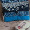 Vue de face d'une pile de pochettes à livre de poche artisanales en coton matelassé bleu avec différents motifs géométriques et fleuris.