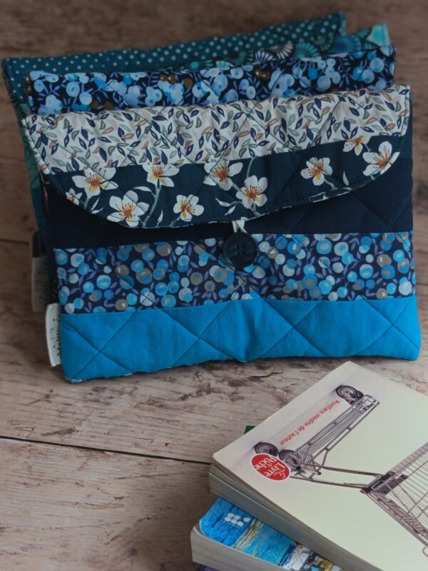 Vue de face d'une pile de pochettes à livre de poche artisanales en coton matelassé bleu avec différents motifs géométriques et fleuris.