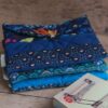 Pile de trois pochettes à livre de poche en tissu matelassé aux nuances de bleu, posée à côté d'un livre de poche.
