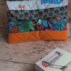 Vue d'ensemble de la pochette à livre de poche originale matelassée orange avec rabat à motifs et bouton en bois.