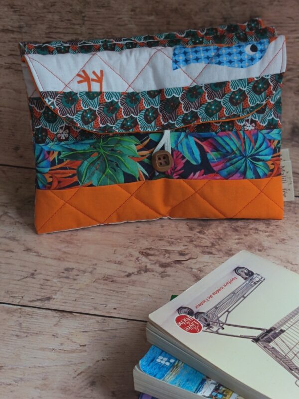 Vue d'ensemble de la pochette à livre de poche originale matelassée orange avec rabat à motifs et bouton en bois.