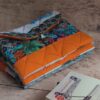 Pochette à livre de poche originale en tissu matelassé orange et motifs tropicaux, posée à côté d'un livre.