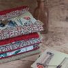 Pile de pochettes à livre de poche tissu matelassées aux nuances de rouge, motifs fleuris et patchwork.
