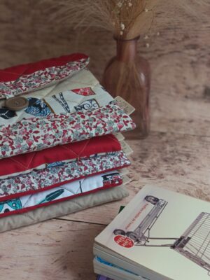 Pile de pochettes à livre de poche tissu matelassées aux nuances de rouge, motifs fleuris et patchwork.
