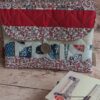 Pochette à livre de poche tissu matelassée rouge et fleurie avec bouton, posée à côté de livres de poche.