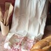 Grand sac à pain réutilisable en coton imprimé toile de Jouy rouge champêtre à côté d'une baguette fraîche.