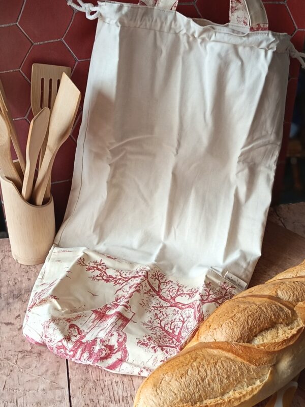 Grand sac à pain réutilisable en coton imprimé toile de Jouy rouge champêtre à côté d'une baguette fraîche.