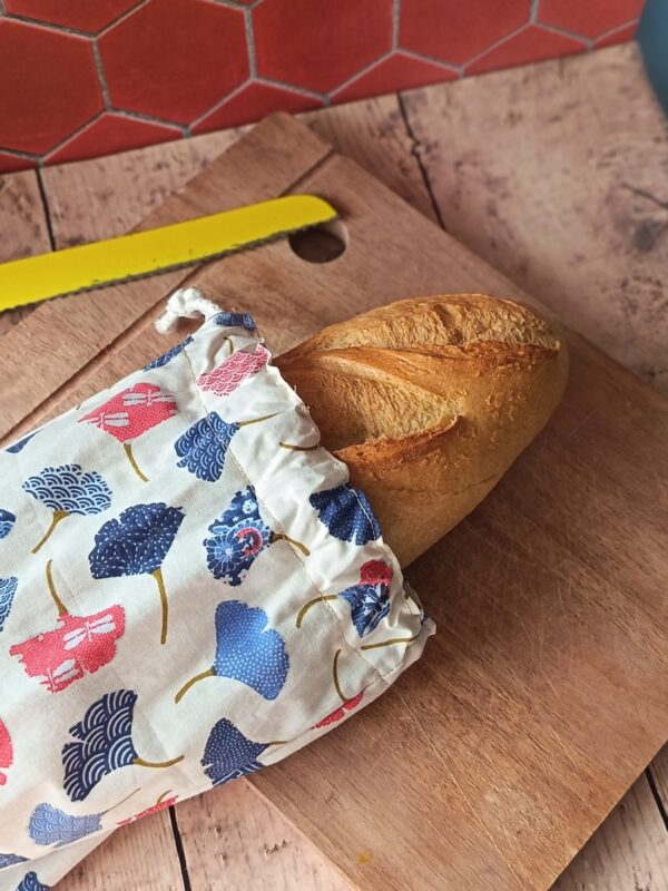 Baguette de pain artisanale dépassant d'un sac à baguette nomade en coton motif ginkgo fermé par un cordon.
