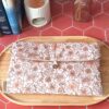 Pochette livre broche tissu matelassée motif Fleur Pastel avec bouton en bois posée sur un plateau