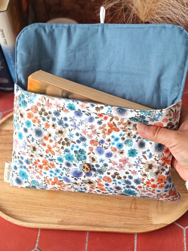 Vue détaillée de la pochette livre broche tissu Hortense Bleu ouverte montrant sa doublure bleue et un roman