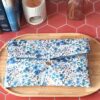 Pochette livre broche tissu matelassée motif Romane aux fleurs bleues et violettes sur plateau en bois