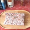 Alt : Pochette livre de poche tissu matelassée motif Fleur Pastel avec bouton en bois posée sur un plateau